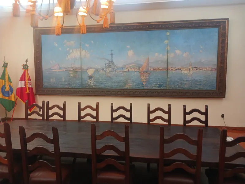 Mesa e cadeiras do Salão Sete de Março diante do tríptico de Navarro da Costa